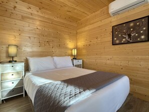 Habitación con paneles de madera, una cama, mesitas de noche y un equipo de aire acondicionado.