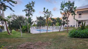Une piscine entourée d’une clôture blanche, avec des palmiers et un bâtiment en arrière-plan.