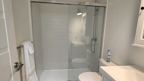 Une salle de bain moderne avec une douche à parois de verre, des toilettes blanches et un lavabo blanc avec un meuble de rangement.