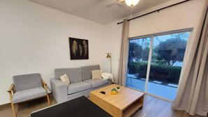 Un salon moderne avec un canapé gris, une table basse en bois et une grande porte-fenêtre coulissante donnant sur un jardin.