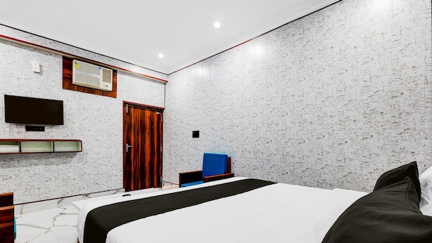 A modern hotel room with a large bed, a flat-screen TV mounted on the wall, a wooden door, and a small desk with a chair.