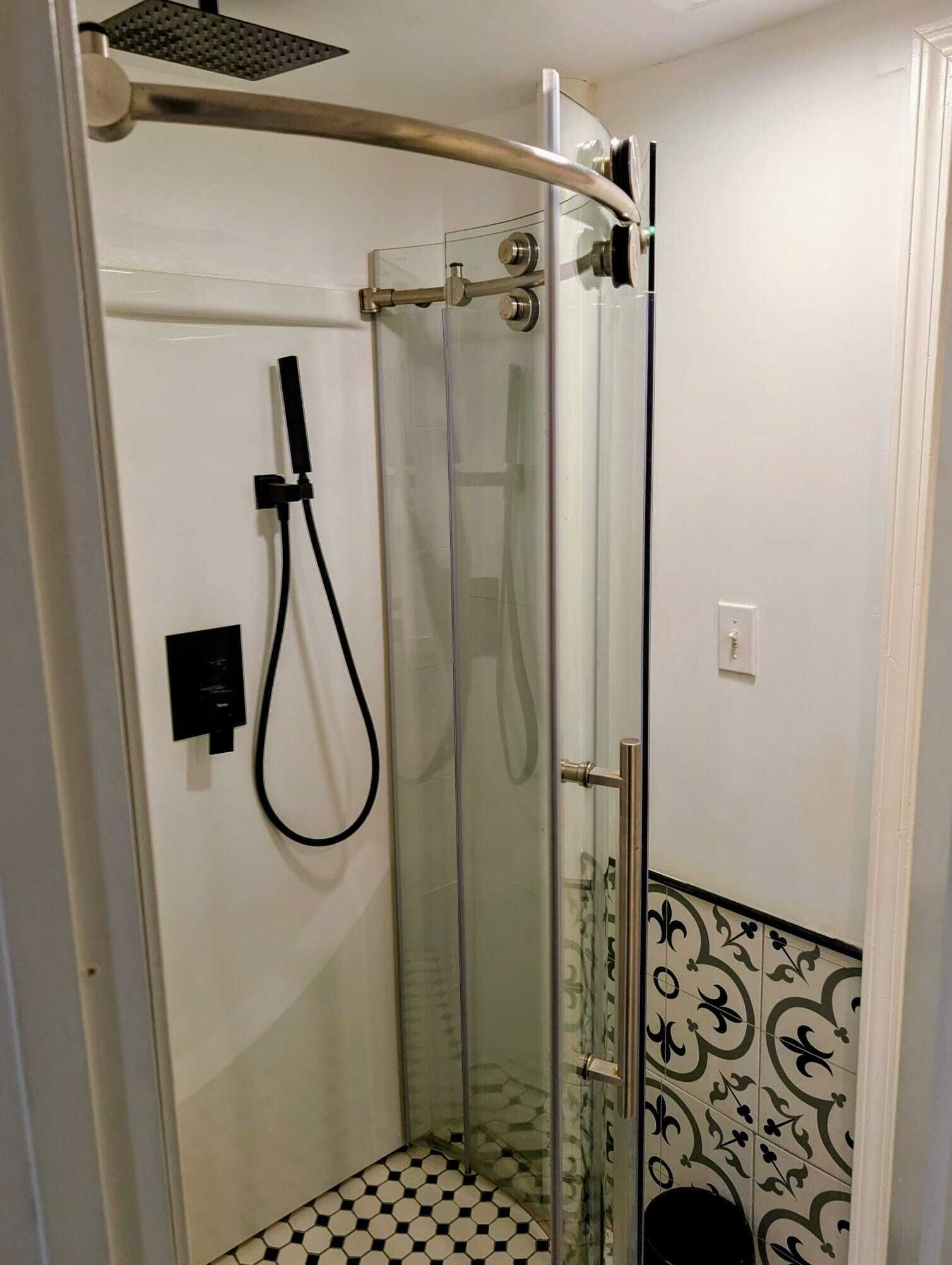 Una ducha con cerramiento de vidrio, cabezal de ducha manual, panel de control y suelo de baldosas.
