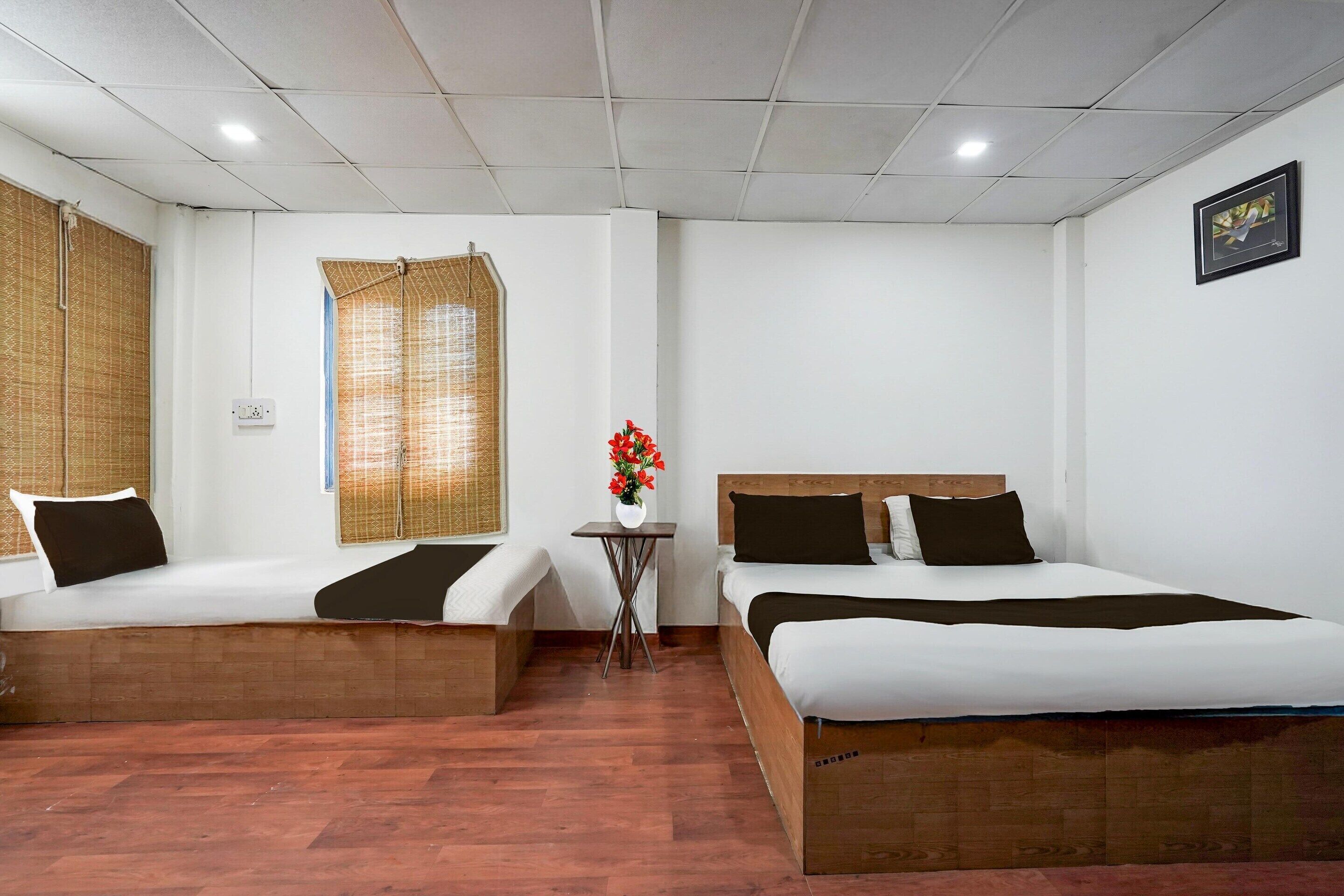 Ein Hotelzimmer mit zwei Betten, einem kleinen Tisch mit Blumenvase und einem Fenster mit Bambusrollos.