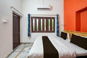 A bedroom with a bed, an air conditioning unit, a window with curtains, a door, and a wall-mounted shelf. - Hotel O Jodhpur Cantt Railway Junction (Jodhpur)