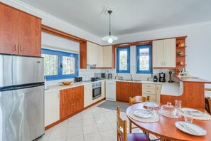 A kitchen with wooden cabinets, a refrigerator, a dining table set for four, and a window with blue shutters.