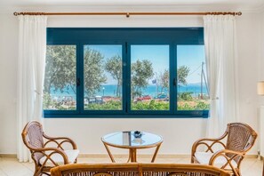 A room with a large window, wicker furniture, and a view of a beach. - Aegean Horizon Karfas – Beachfront Living, Open Sea Views, Pure Aegean Calm (Chios)