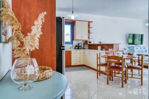 A dining area with a table, chairs, and a television in the background. - Aegean Horizon Karfas – Beachfront Living, Open Sea Views, Pure Aegean Calm (Chios)