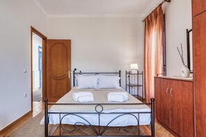 A single bed with a metal frame, a wooden wardrobe, and a door leading to another room. - Aegean Horizon Karfas – Beachfront Living, Open Sea Views, Pure Aegean Calm (Chios)