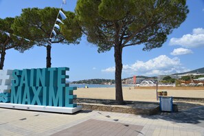 Ein Schild am Strand mit der Aufschrift "SAINTE MAXIME", eine Steinmauer und ein klarer, blauer Himmel.