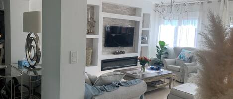 Un salon moderne doté d’un téléviseur à écran plat, d’une cheminée, d’un canapé, d’une table basse et d’un lustre.