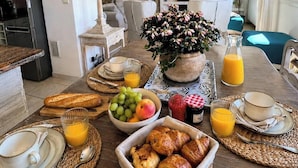 A breakfast table with bread, fruits, and beverages, a potted plant, and a TV in the background. - Very Nice 3-Room Apartment, 84 m2, Spacious, Saint-Maxime, Beach 300 Meters Away (Sainte-Maxime)