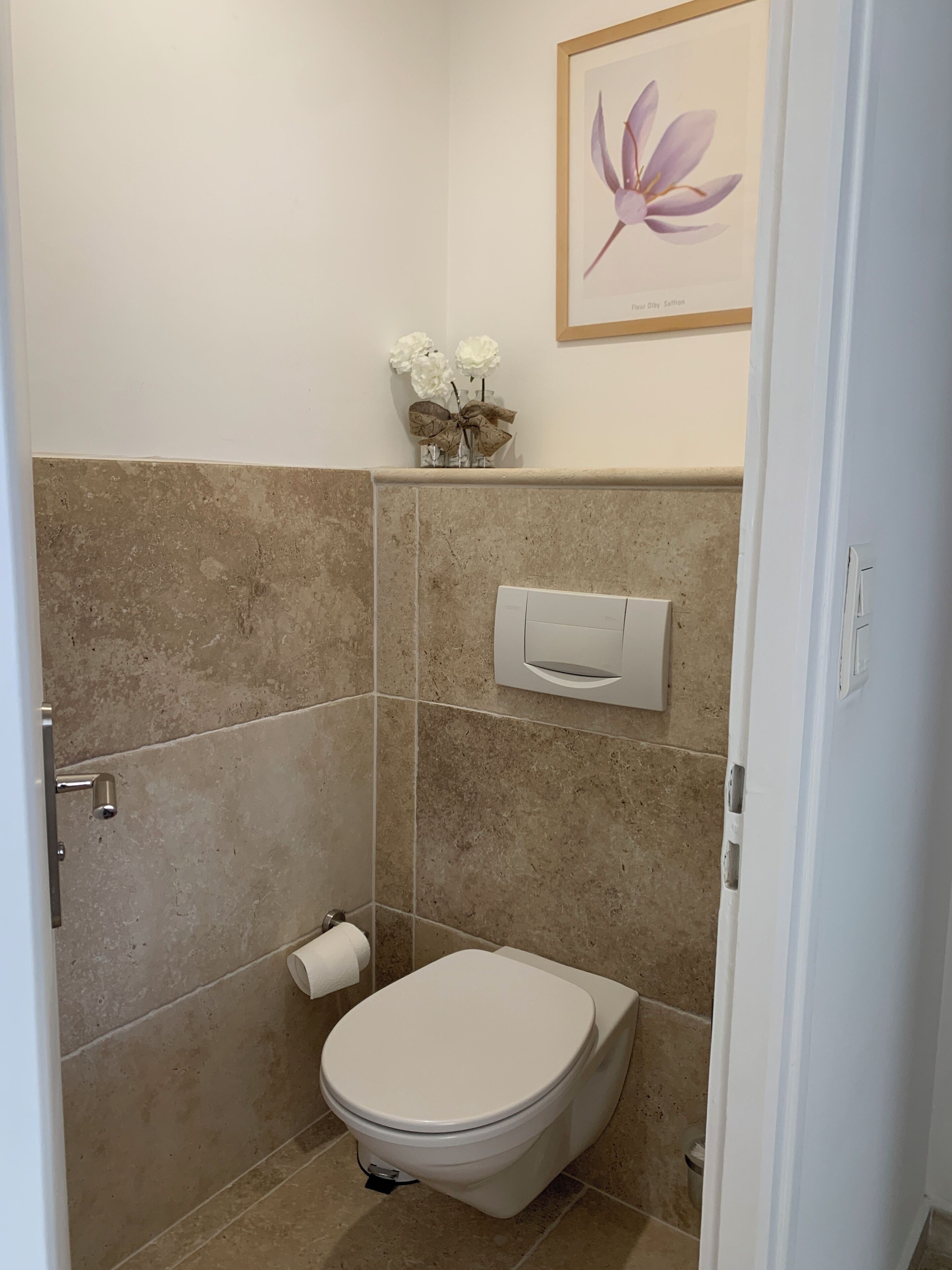 Une salle de bain équipée de toilettes, d’un distributeur de serviettes et d’une œuvre d’art florale encadrée au mur.