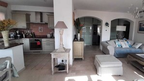 A spacious living area with a sofa, ottoman, and a television. A kitchen is visible in the background with modern appliances. - Very Nice 3-Room Apartment, 84 m2, Spacious, Saint-Maxime, Beach 300 Meters Away (Sainte-Maxime)
