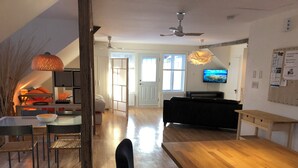 Een moderne woonkamer met een houten eettafel, een zwarte bank en een televisie aan de muur.