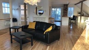 Een moderne woonkamer met een zwarte leren bank, een klein zwart tafeltje en een unieke witte hanglamp.