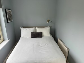 A neatly made bed with white bedding, a single dark pillow, and a bedside lamp. - Bright 2BDR Home in Blackrock Cork (Cork)