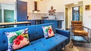 Una sala de estar moderna con un sofá azul, una silla de madera y una cocina al fondo.