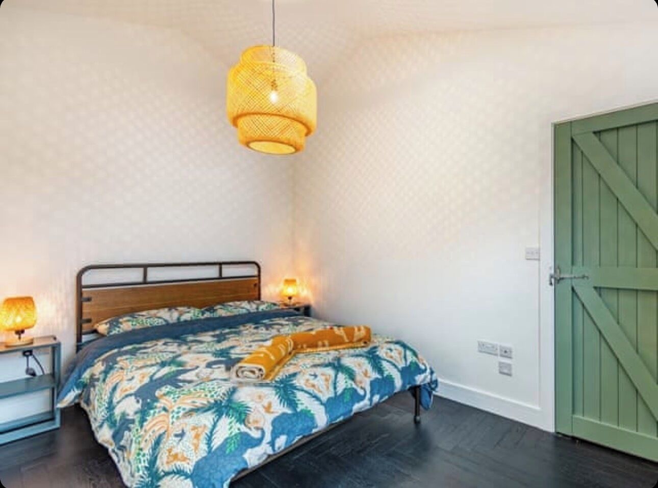 A bedroom with a bed, a nightstand, a lamp, and a green door.