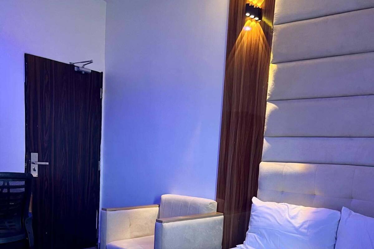 Een hotelkamer met een groot bed, twee fauteuils, een houten deur en een wandlamp.