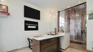 A modern reception desk with a white top and wooden base, a mounted TV, and a sign reading "TOWNHOUSE Company-Serviced".