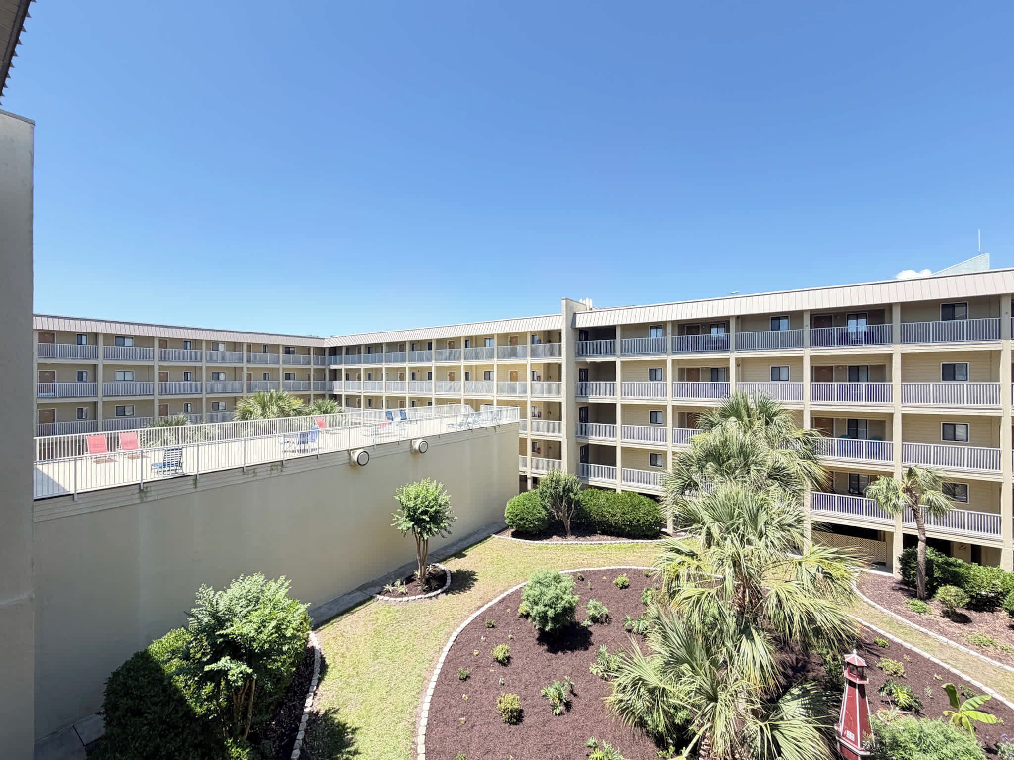 Un hôtel à plusieurs étages doté de balcons, une cour intérieure aménagée et un ciel d’un bleu éclatant.