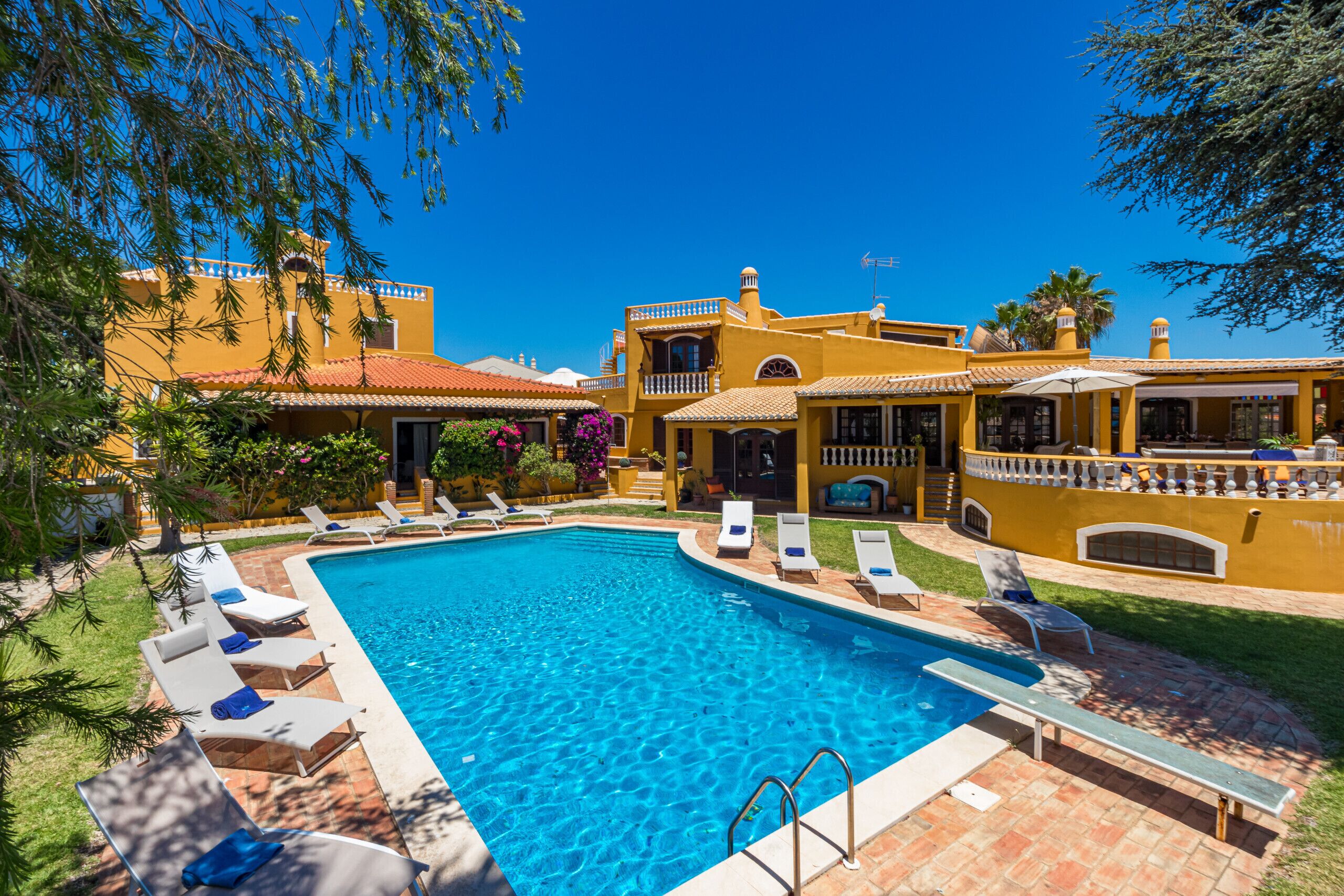 Una piscina con sillas de descanso y un edificio amarillo con balcón.