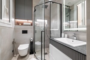 Un baño moderno con ducha envuelta en vidrio, inodoro blanco y un lavamanos grande con espejo arriba.