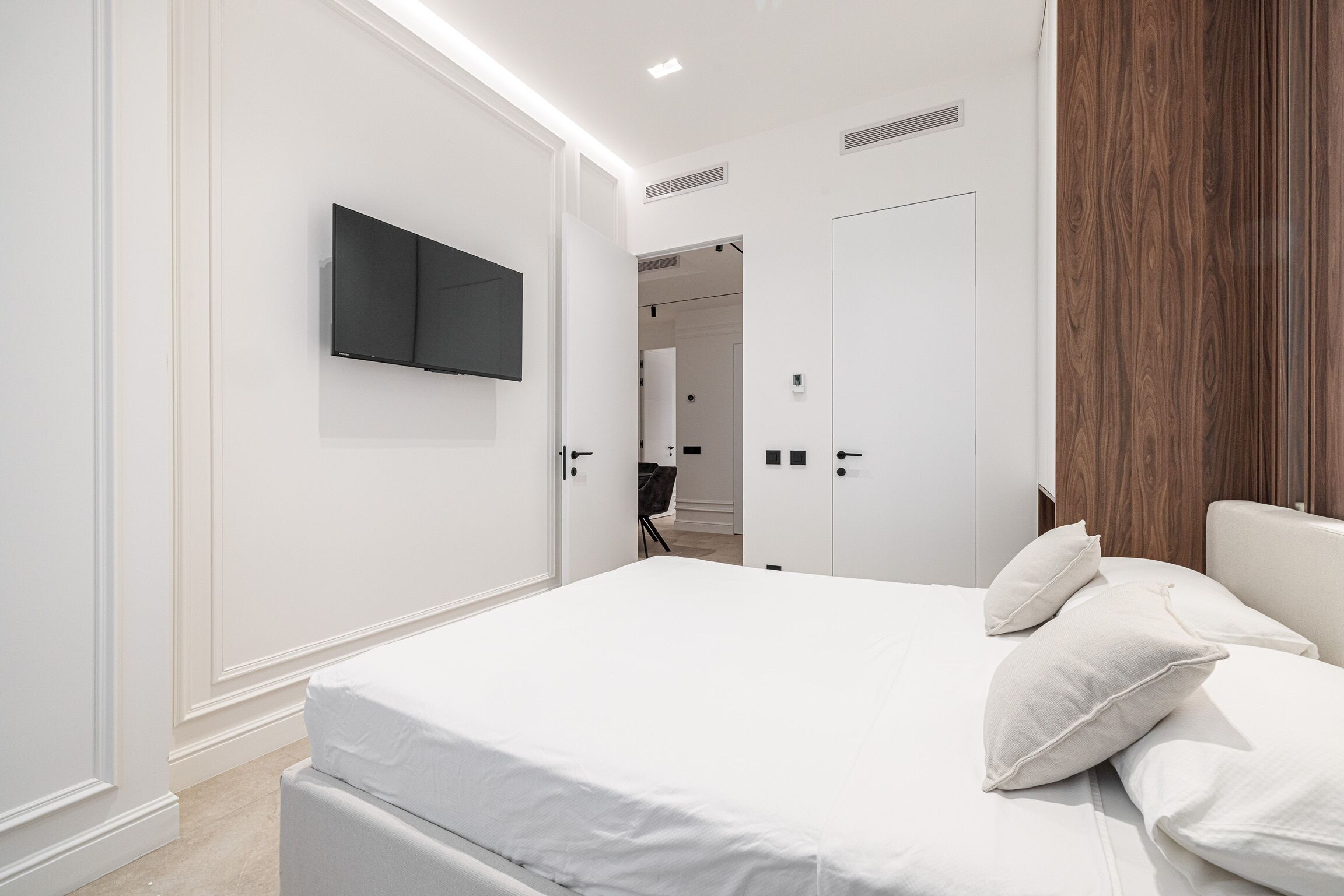 Een moderne slaapkamer met een groot bed, een flatscreen televisie aan de muur en een houten paneel aan de rechterkant.