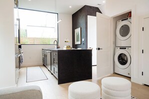 A modern kitchen with a black countertop, a built-in oven, and a window. There are two white ottomans and a washing machine visible. - Stylish 2BR Zilker/Barton Springs Home.  Walkable, Modern, True Austin Vibes!! (Austin)