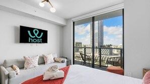 Une chambre d’hôtel moderne dotée d’un grand lit, d’un canapé, d’un téléviseur fixé au mur et d’un balcon offrant une vue sur la ville.