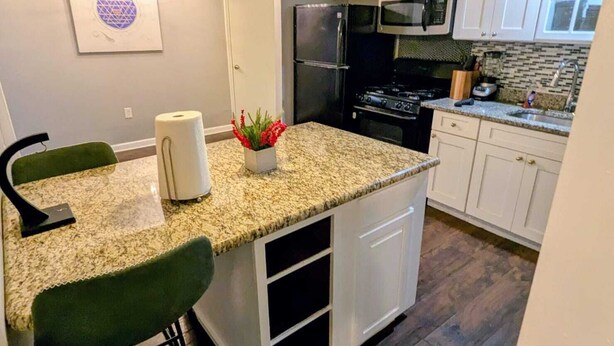 Una cocina moderna con armarios blancos, encimera de granito, refrigerador de acero inoxidable y microondas.