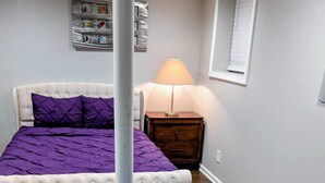 Un dormitorio con una cama capitonada, una mesita de noche, una lámpara y una alfombra estampada.