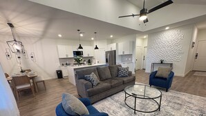 Uma sala de estar moderna com um sofá cinza, poltronas azuis e uma mesa de centro de vidro.