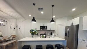 Cozinha moderna com ilha central, banquetes pretos, armários brancos e eletrodomésticos de aço inoxidável.