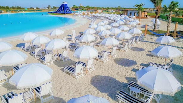 Um resort à beira-mar com uma piscina grande, vários guarda-sóis brancos e espreguiçadeiras.