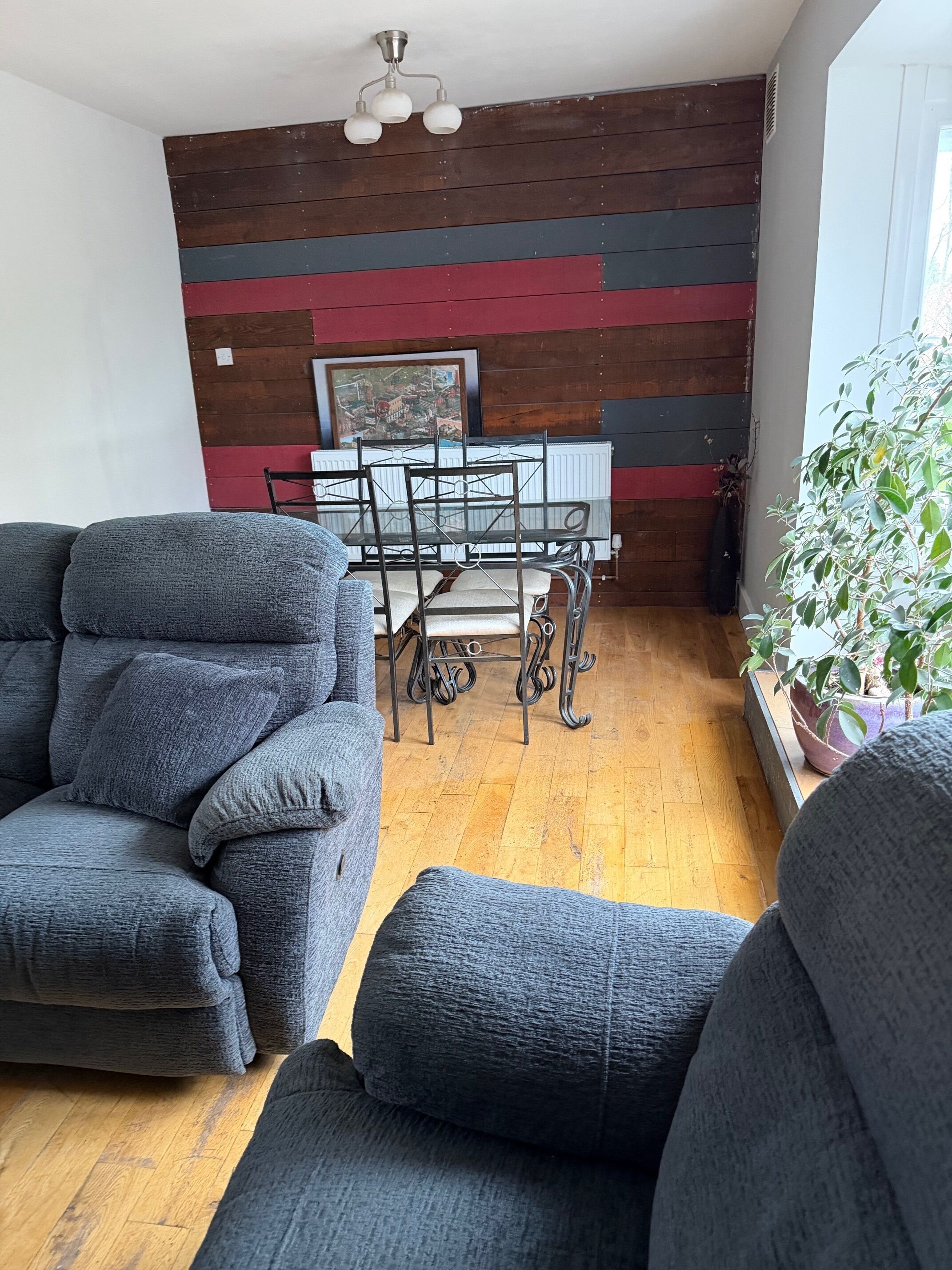 A cozy living room with a gray sofa set, a wooden floor, and a dining table with chairs.