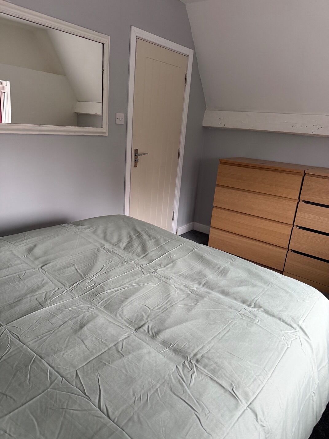 A bedroom with a bed, a dresser, a door, and a mirror on the wall.