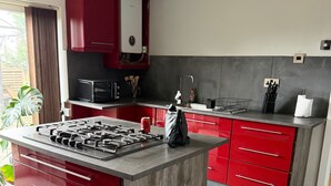 A modern kitchen with red cabinetry, a central island with a gas stove, and a microwave above the sink. - Charming Birmingham 3 Bedroom Apartment (Birmingham)