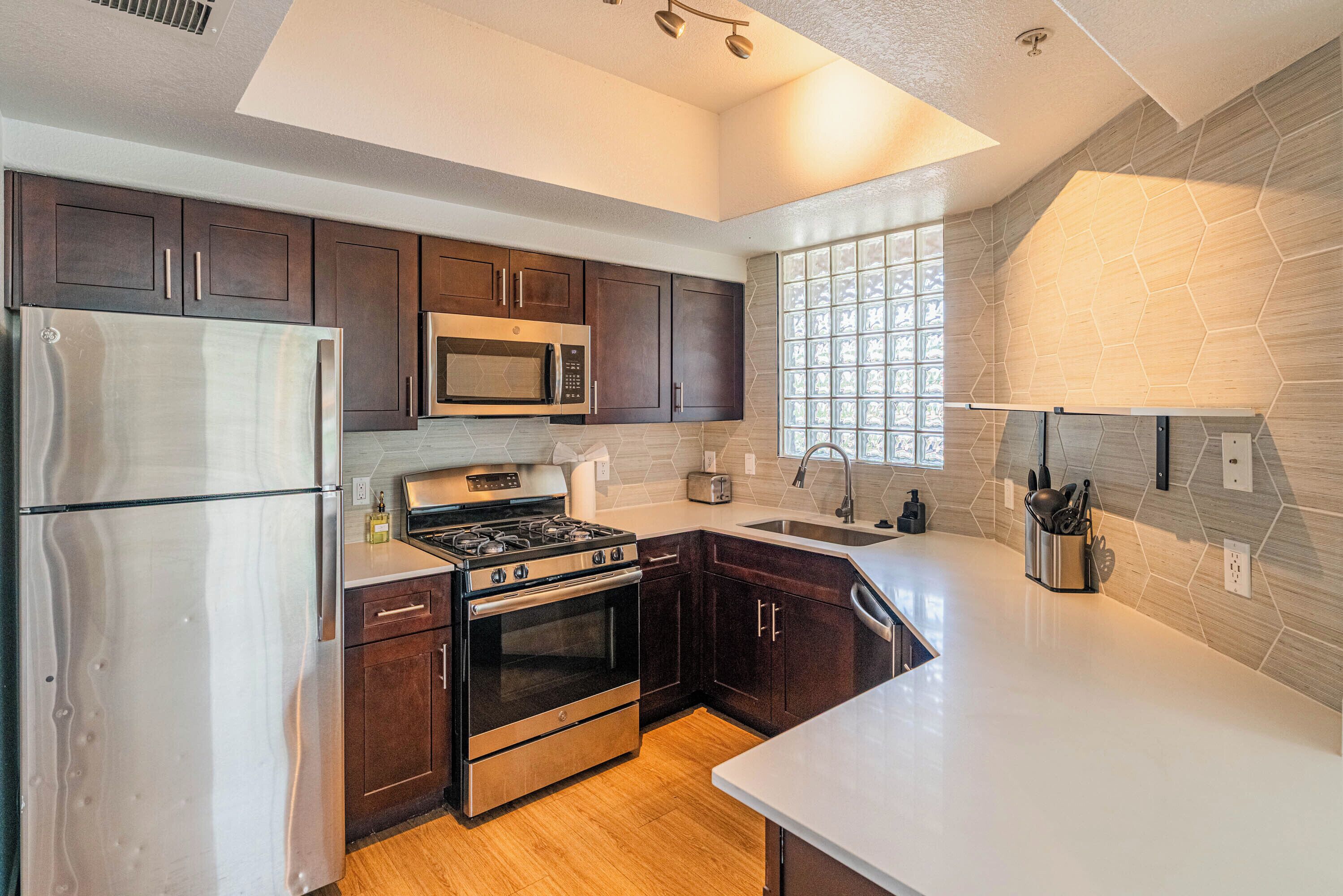 A modern kitchen with dark wooden cabinets, stainless steel appliances, and a large window providing natural light.