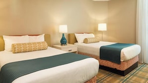A hotel room with two beds, each with a white bedspread and a teal blanket. There are two bedside tables with lamps, and the room has a plaid carpet. - Wyndham ON THE BEACH 3-BR condo in beautiful North Myrtle Beach, LAZY RIVER! (North Myrtle Beach)