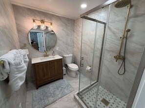 Une salle de bain moderne dotée d’une douche à parois de verre, d’un sol carrelé en marbre, d’un meuble-lavabo en bois et d’un grand miroir rond agrémenté de luminaires suspendus.