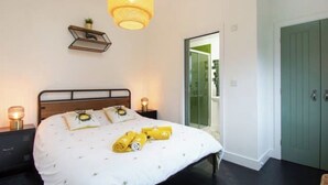A bedroom with a bed, bedside lamps, a hanging light fixture, a small shelf with a plant, and a sliding glass door leading to a balcony. - Diesel's Desirable Den - Luxury rural 2 bed cottage, peaceful walks and stays UK (Maidstone)