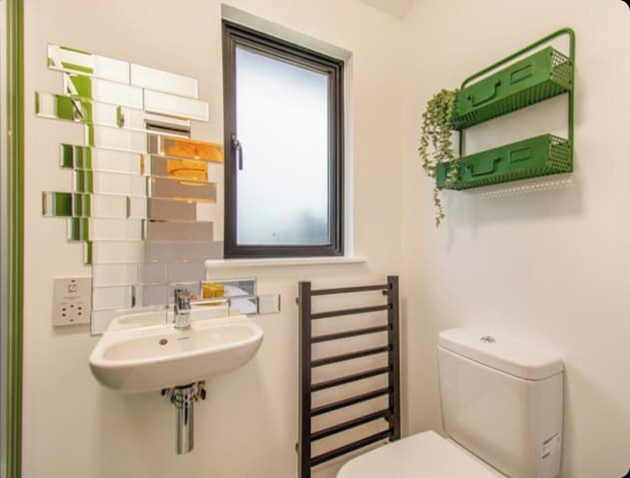 Un baño con lavamanos blanco, una ventana sobre el espejo, un perchero para toallas y un inodoro.