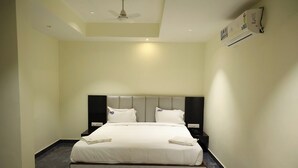 A hotel room with a bed, a ceiling fan, an air conditioning unit, and a nightstand with a phone. - Hotel DP's Crown (Bengaluru)