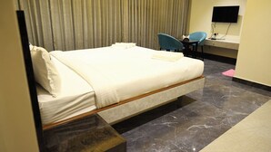 A hotel room with a bed, a desk with a chair, a flat-screen TV, and a curtain. - Hotel DP's Crown (Bengaluru)