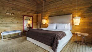 Un dormitorio con paneles de madera, una cama grande, un banco y una mesita.