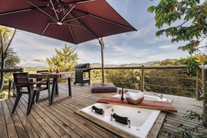 Una terraza de madera con un jacuzzi, una mesa con sillas y un paraguas grande.