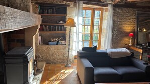 A rustic room with a stone wall, a fireplace, a sofa, and a bookshelf. - Charming stone house in P érigord • Peaceful • Garden • 8 guests (Coulaures)