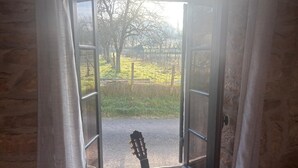 A doorway with a guitar leaning against it, leading to a grassy outdoor area with trees and a fence. - Charming stone house in Périgord • Peaceful • Garden • 8 guests (Coulaures)