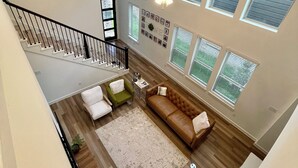 A spacious living area with a staircase, wooden flooring, a brown leather sofa, a green armchair, and a white armchair. - Wonderful 4-bedroom house with AC in tranquil Houston neighborhood (Houston)